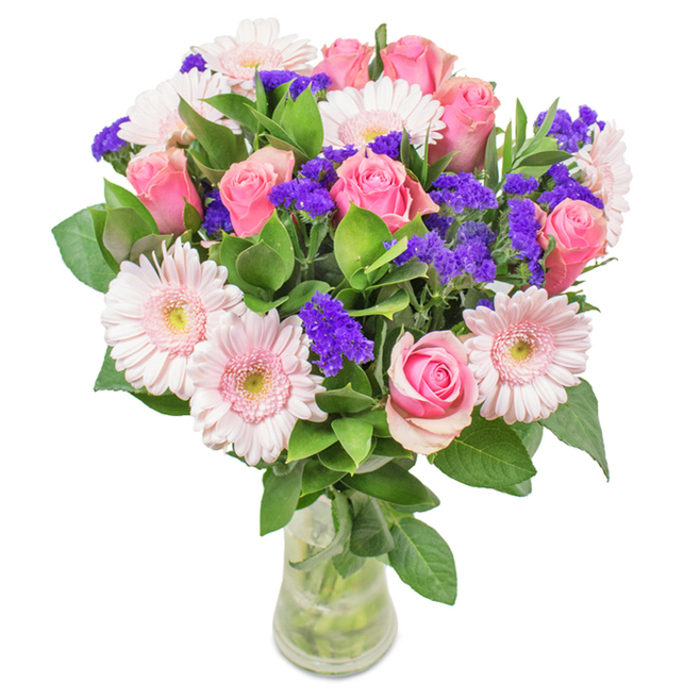 This sophisticated bouquet, displayed in a clear glass vase upon a pristine white backdrop, captures the creative spirit of Florist White City and echoes the vibrant heart of the local community. At its centre, 7-9 blushing pink roses-some tightly furled, others just beginning to reveal their classic spiral petals-join with 5-7 pale gerbera daisies, each with round, radiating petals and nearly white-centred faces. Bright purple statice, artfully placed among the main blooms, add lively pulses of colour and rich, papery texture, gently echoing the season's wildflowers around White City Green. Lush, deep green foliage envelops the composition, providing a sense of abundance and fresh vibrancy inspired by the leafy avenues nearby. The transparent vase holds visible stems and crystal-clear water, a perfect finishing touch that hints at same-day freshness. This bouquet, ideal for birthdays, anniversaries, Mother's Day, or uplifting home and office spaces across White City, radiates celebration, affection, and handcrafted joy-carefully assembled for those who value both beauty and meaning.